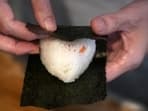 A person wraps seaweed around a rice ball to make onigiri. The humble sticky-rice ball, a mainstay of Japanese food, has entered the global lexicon. 